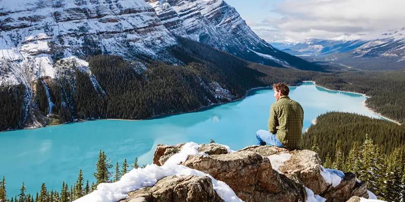 Young man sitting on a mountain slope enjoying the view of mountains and a lake